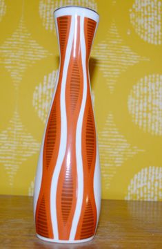 an orange and white vase sitting on top of a wooden table next to a yellow wall