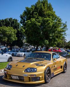 a yellow sports car parked in a parking lot next to trees and other cars on the street