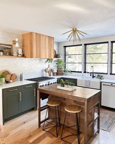 a kitchen with wooden floors and green cabinets, an island in the middle is surrounded by stools