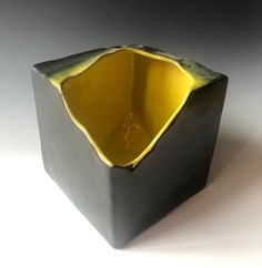 a black vase with yellow interior on a white surface