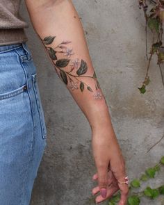 a woman's arm with flowers on it and leaves in the middle, while she is holding her hand out