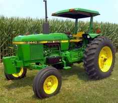 a large green tractor parked in front of a corn field with yellow wheels on it