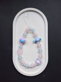 a white tray holding a pink and blue beaded bracelet with heart shaped charms on it