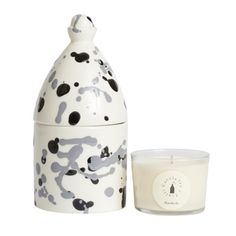 a candle next to a ceramic jar with black and white designs on it, sitting beside a glass container