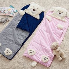 two teddy bears laying on the floor next to a sleeping bag