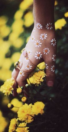 a woman's hand with white and yellow flowers painted on her left arm, holding onto some yellow flowers