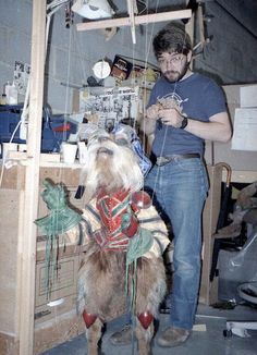 a man standing next to a stuffed animal on top of a wooden table in a room