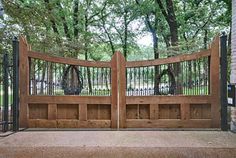 a wooden gate with metal railings in front of a brick wall and tree - lined area