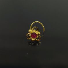 a gold ring with a red stone in the middle on a black surface, it is set against a dark background