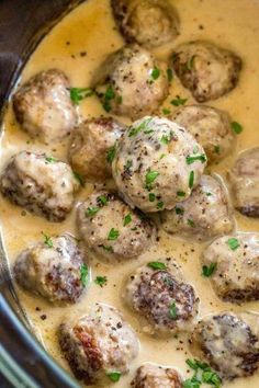 a crock pot filled with meatballs covered in gravy and garnished with parsley