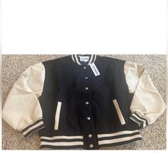 This Stylish Black "Alexandra" Varsity Jacket Is Perfect For Any Fashion-Forward Woman Who Wants To Make A Statement. Made From High-Quality Polyester, This Jacket Is Designed To Last And Keep You Warm At The Same Time. The Jacket Features A Snap Closure, Making It Easy To Put On And Take Off. The Steve Madden Brand Is Known For Its Trendy And Fashionable Clothing, And This Bomber Jacket Is No Exception. Designed For Juniors, This Jacket Is Perfect For College Or Greek School-Themed Events. It H Fall Beige Outerwear For College, Cream Long Sleeve Varsity Jacket For Fall, Trendy Cream Outerwear For Streetwear, Long Sleeve Varsity Jacket For Workwear, Cream Outerwear For College In Fall, Fall Cream Outerwear For College, Cream Fall Outerwear For College, Black Oversized Varsity Jacket For College, Black Varsity Jacket With Contrast Collar For College