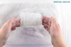 two hands holding a roll of toilet paper on top of a white sheet covered in tiny speckles