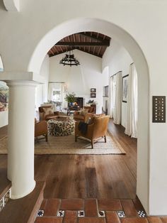 a living room with wooden floors and white walls, arched doorway leading into the dining area