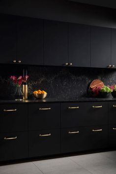 a kitchen with black cabinets and gold handles on the counter tops, along with bowls of fruit and vegetables