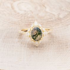 a ring with a large green stone surrounded by small white and yellow diamonds on a wooden surface