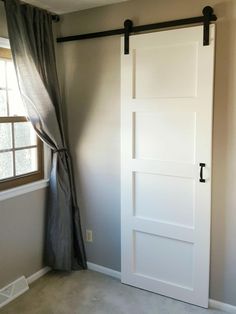 an empty room with a white door and curtains on the window sill next to it