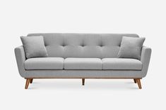 a grey couch with two pillows on it and some wooden legs, against a white background