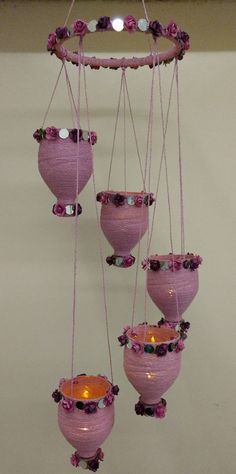 a group of pink vases hanging from a string with flowers on them and some lights in the middle