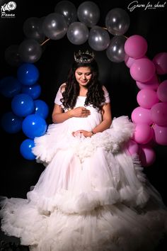 a pregnant woman wearing a tiara and dress in front of balloons