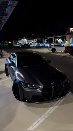 a black sports car parked in a parking lot at night with its hood up and lights on