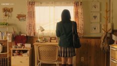 a woman standing in front of a window next to a desk with a computer on it