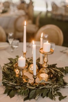 candles are lit on a table with greenery