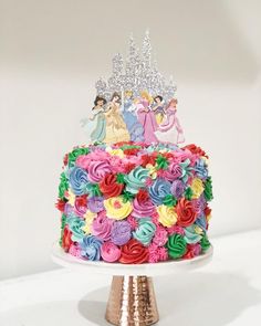 a multicolored birthday cake with princess figures on top and flowers in the middle