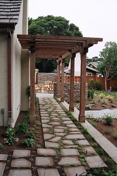 an outdoor patio with stone walkway and pergolated seating area next to the house