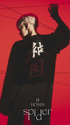 a man standing in front of a red wall wearing a black shirt with writing on it