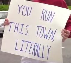 a man holding a sign that says you run this town literally