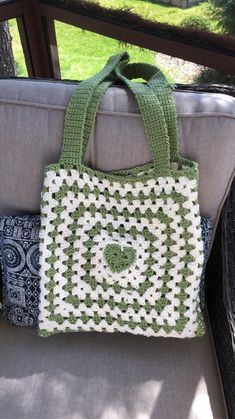 a green and white crocheted bag sitting on top of a gray couch next to a tree