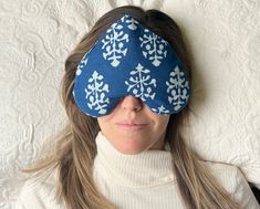 a woman laying on top of a bed wearing a blue eye mask