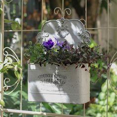 a white planter filled with purple flowers sitting on top of a metal trellis