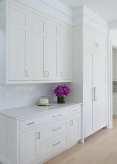 a kitchen with white cabinets and purple flowers in a vase on the counter top next to an oven