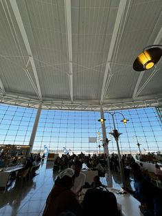 people are sitting at tables in an airport terminal with large windows on the wall and ceiling