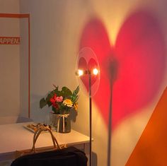 a heart - shaped light is on the wall next to a bag and flowers in a vase