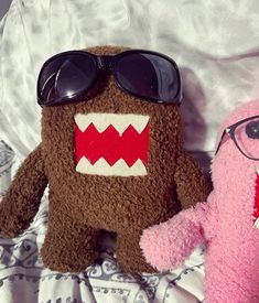 two stuffed animals wearing sunglasses on top of a white bed sheet with a pink teddy bear in the foreground