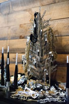 a small christmas tree is surrounded by chains and other decorations on a table in front of a wooden wall