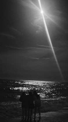 black and white photograph of three people standing on the beach at night with bright sun in background