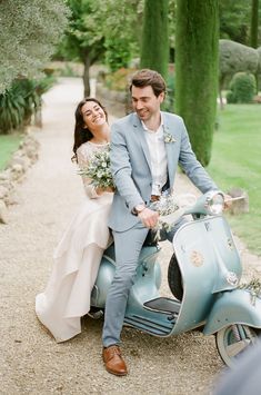 a bride and groom sitting on a scooter in the middle of a path