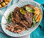 steak and potatoes on a white plate next to a glass of water with a blue cloth