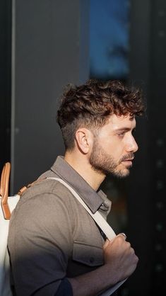 Moving to a more bohemian vibe, the man in showcases a wavy shag that's all about movement and depth. This hairstyle for men is for those who carry a rebel spirit and aren't afraid to let their hair make a statement. The layers create a dynamic silhouette, while the waves add a rugged yet romantic charm that's undeniably compelling. Thick Curly Hair Men Style, Men’s Short Curly Hair Styles, Undercut Hairstyle Men Curly, Mens Curly Haircuts Fade, Men's Curly Hairstyle, Classic Curly Hairstyles Men, Mens Thick Curly Hairstyles, Men Haircut For Curly Hair, Curly Hair Men Haircut Taper