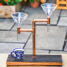 two coffee cups sitting on top of a wooden table next to a copper faucet