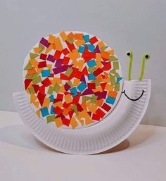 a paper plate with a snail made out of small pieces of colored paper on it