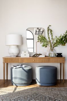 a table with two stools and a mirror on it next to a plant in a vase