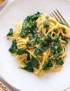 pasta with spinach and parmesan cheese on a white plate next to silverware