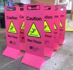 three pink caution signs sitting next to each other on top of a floor in front of a building