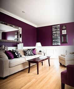 a living room with purple walls and white furniture in the center, along with a large mirror on the wall