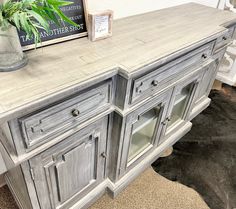 an old gray buffet with glass doors and drawers on display in a store or showroom