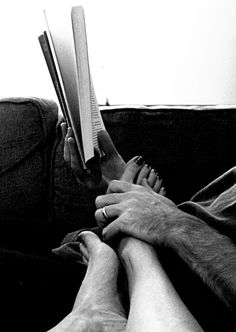 two people sitting on a couch with their legs crossed and reading the same book together